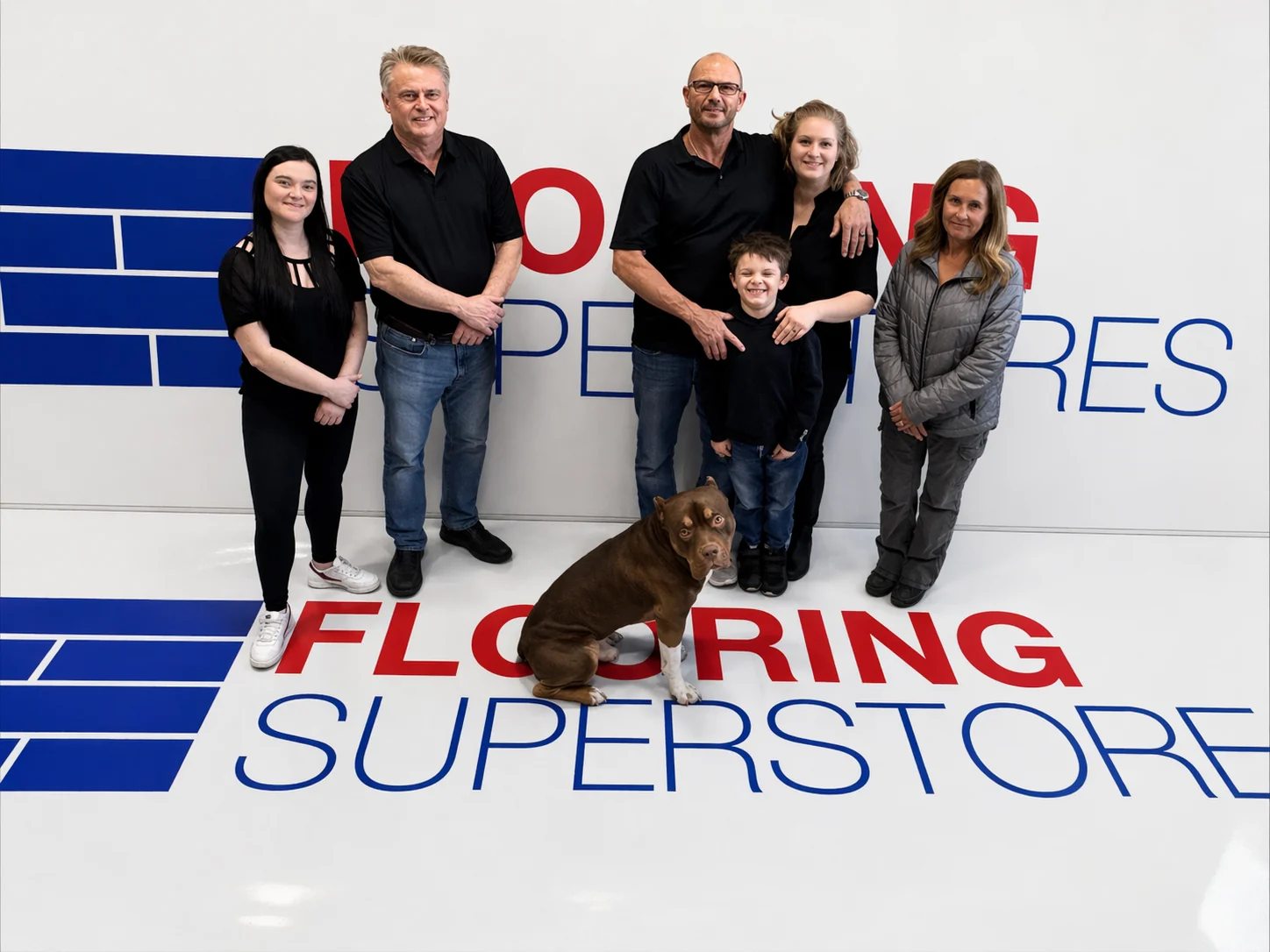 Kelowna Flooring Superstore team — showroom staff, installers, and shop dog in front of the Flooring Superstores mural